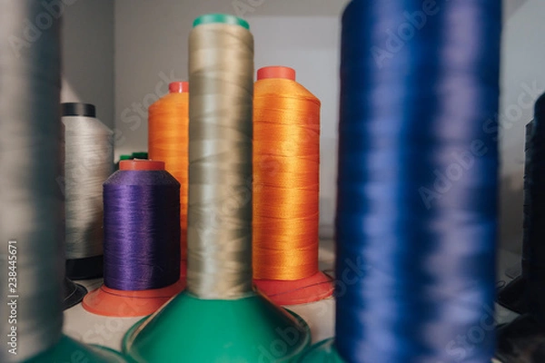 Fototapeta Close up detail shot of threads in a shelf. Sewing threads on a spool, yarn on plastic tubes. Material for sewing.