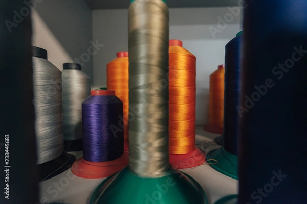 Fototapeta Close up detail shot of threads in a shelf. Sewing threads on a spool, yarn on plastic tubes. Material for sewing.