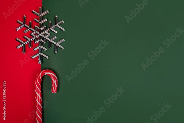 Fototapeta Christmas flatlay with candy canes and silver snowflake on the bright red and green background.