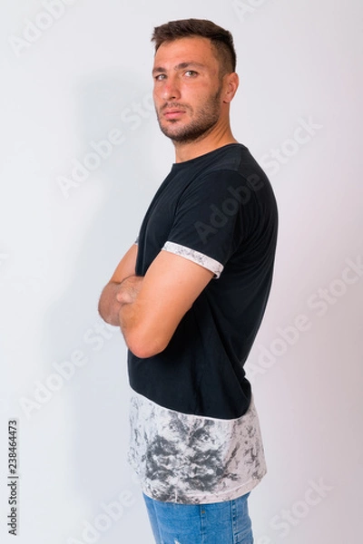 Fototapeta Profile view of handsome bearded Persian man looking at camera with arms crossed