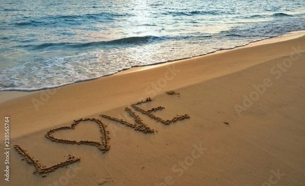 Fototapeta Valentines day concept, love heart shape handwriting on sand beach in sunrise and blue ocean.