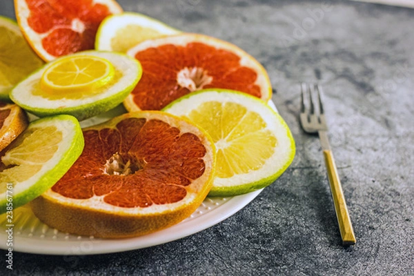 Fototapeta Rings of grapefruit and pomelo on a plate of different colors, next to a fork. Background with citrus. Background with grapefruit