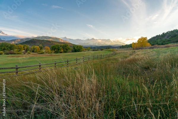 Fototapeta The sun is about to set over a ranch in the colorado mountains filled with cows and surrounded by fences