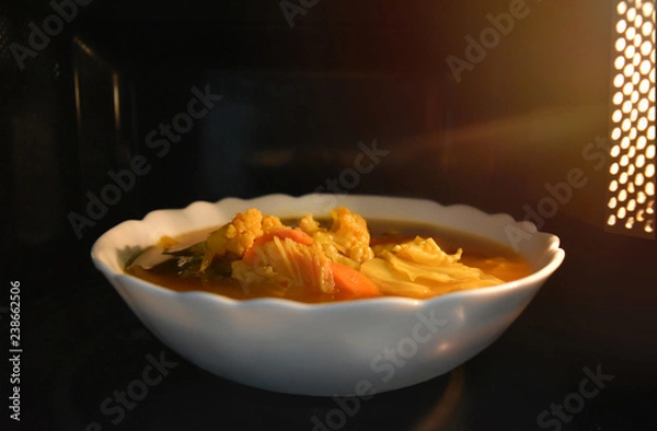 Fototapeta Look inside the microwave food white bowl, In a warm atmosphere and empty top space for text. (Spicy food). Non color ceramic applicable to available with microwave.