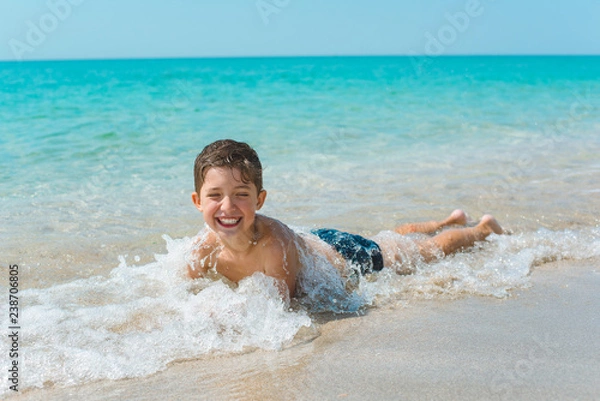 Obraz A cheerful kid on the beach lies in the clear sea water.