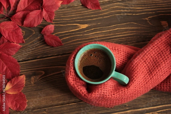 Obraz Coffee in a blue mug, wrapped in a warm scarf and red leaves on a wooden table.