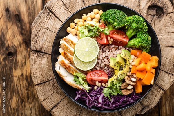 Obraz Sałatka Buddha Bowl z filetem z kurczaka, brązowym ryżem, awokado, papryką, pomidorem, brokułami, czerwoną kapustą, ciecierzycą, świeżą sałatą, orzeszkami pinii i włoskimi. zdrowe jedzenie. zbilansowana dieta. Widok z góry