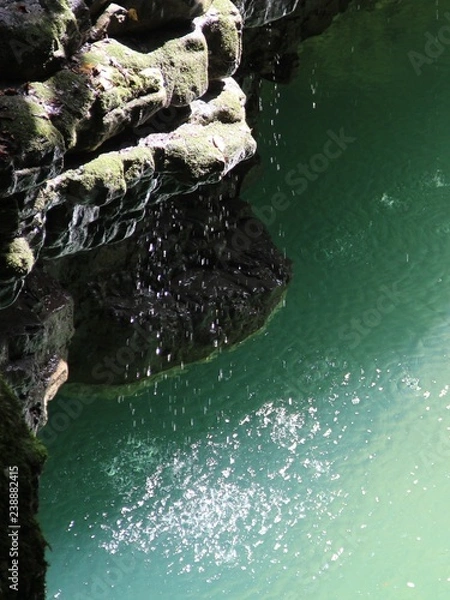 Fototapeta water drops fall from a stone cliff into a river