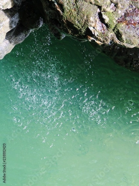 Fototapeta water drops fall from a stone cliff into a river