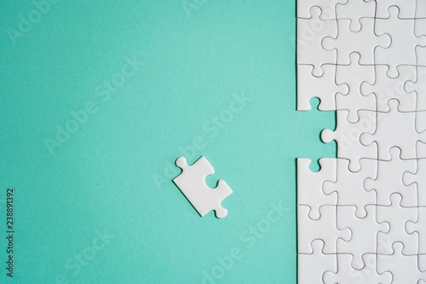 Fototapeta Fragment of a folded white jigsaw puzzle and a pile of uncombed puzzle elements against the background of a colored surface.