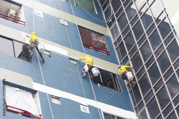 Fototapeta painters hanging on roll, painting color on building wall.