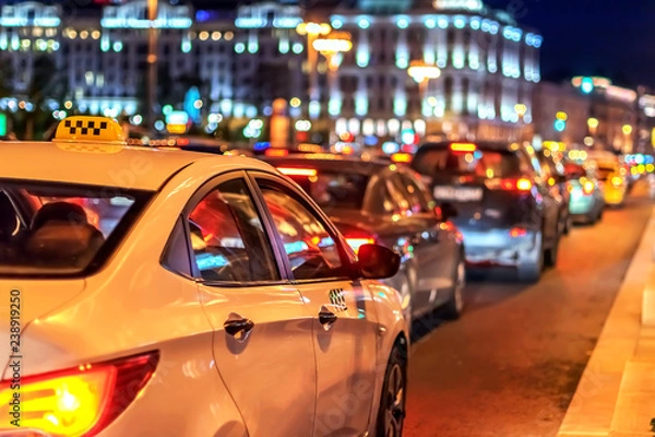 Fototapeta taxi in traffic jam among street cars in the evening rush hour in megalopolis on background of lights of the night city and bokeh