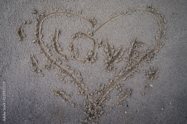 Fototapeta Heart is drawn in the sand of a beach by a stick in the center of the inscription love.