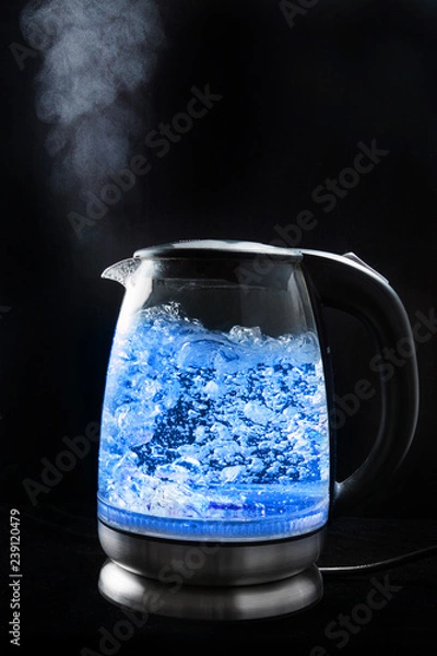 Fototapeta Boiling glass kettle with blue light on a black background, steam comes from the spout