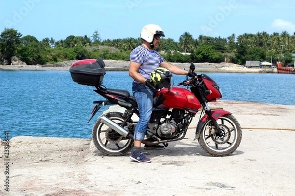 Fototapeta Biker on the background of the sea with a helmet in hand