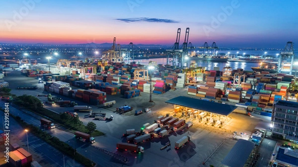 Fototapeta Container truck go to terminal container warehouse at seaport with crane bridge loading container to container ship at dusk for logistics import export or transportation.