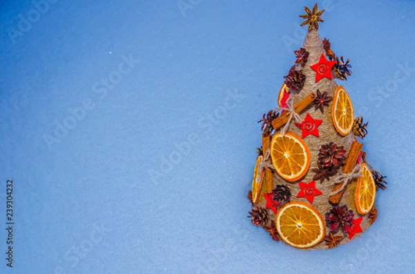 Obraz Необычная новогодняя ель, выполненная в стиле «арт-деко» украшенная сушеными апельсинами, сосновыми шишками, бадьяном, корицей и расположенной на снежном покрове.