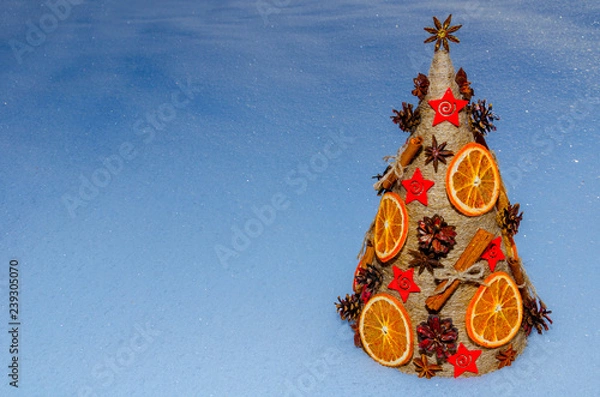 Obraz  Необычная новогодняя ель, выполненная в стиле «арт-деко» украшенная сушеными апельсинами, сосновыми шишками, бадьяном, корицей и расположенной на снежном покрове.