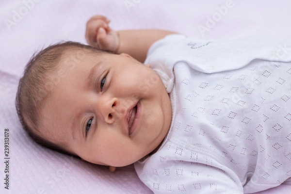 Fototapeta The baby lies on a pink background with a raised hand and crossed fingers, shows a bright emotion.