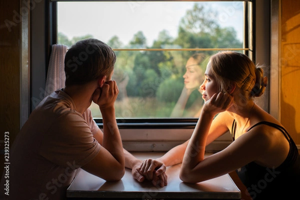 Obraz Couple of lovers traveling in train. Mood portrait of romantic pair in wagon looking at window with self reflections in it. Adventure on holiday of happy friends. Man and woman looking at each other.