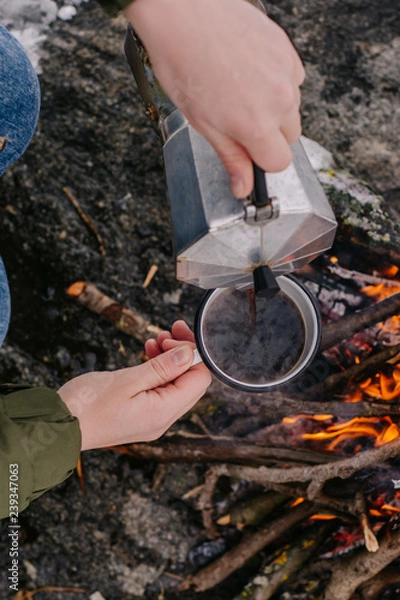 Obraz Traveling-woman  a  sits near camp fire an in winter time and pours itself hot coffee . Concept adventure active vacations outdoor. Winter camping