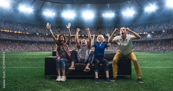 Obraz Group of students are watching a soccer moment, sitting on the couch located in the middle of the soccer stadium.
