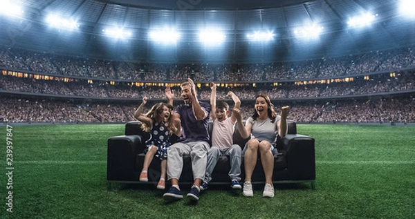 Obraz A family is watching a soccer moment, sitting on the couch located in the middle of the soccer stadium.