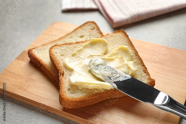 Fototapeta Spreading butter onto toast with knife on wooden board