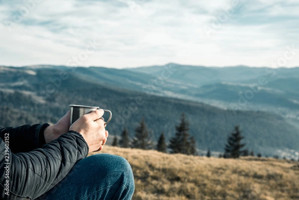 Fototapeta a man with a metal cup sits on a background of mountains