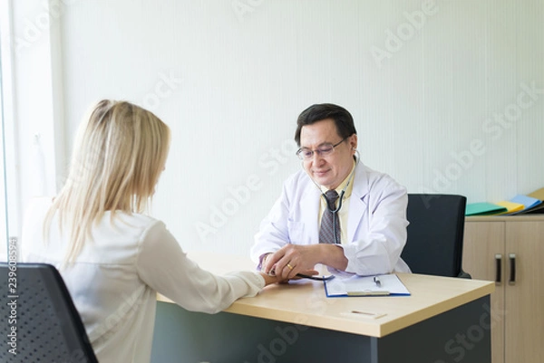 Fototapeta Doctor using stethoscope to woman patient for listening heart rate on sickbed at hospital