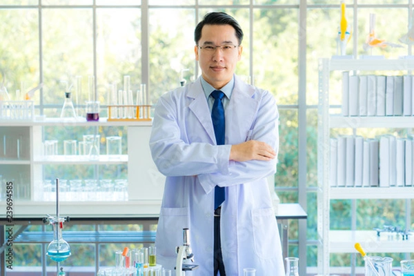Fototapeta A middle aged man scientist smiling happily with his arms crossed posing at her laboratory colleagues. A confident professor CEO standing preparing equipment for teaching collage student. Copy space.