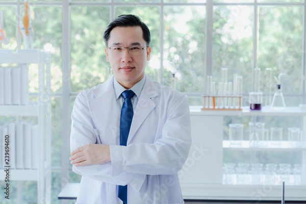 Obraz A middle aged man scientist smiling happily with his arms crossed posing at her laboratory colleagues. A confident professor CEO standing preparing equipment for teaching collage student. Copy space.