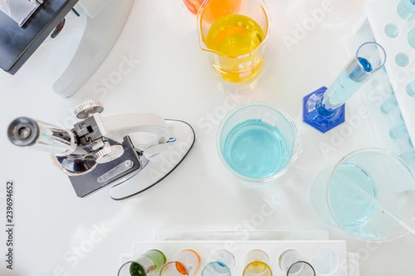 Fototapeta Closed up microscope with tube glass and beaker in laboratory. Blue chemist in glass tubes on white table. Top view of lab in experiment for biotechnology and pharmacy for human life concept.