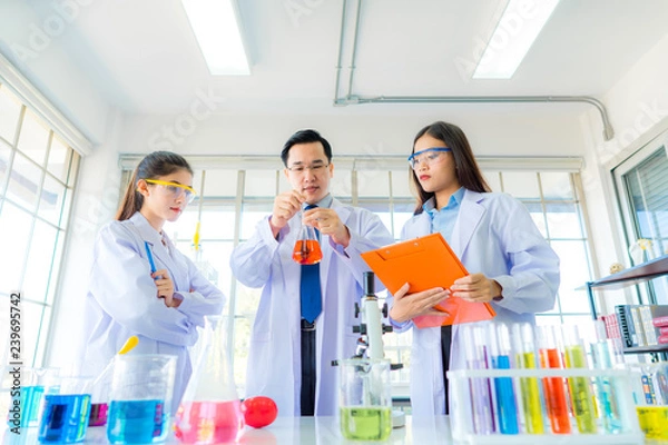 Obraz A handsome professor checking liquid in beaker for young beautiful asian woman scientist watching substance in chemistry experiment in hospital lab. Portrait of science & healthcare concept.