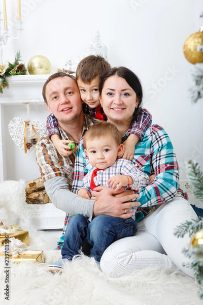 Fototapeta Parents and two little children having fun and playing together near Christmas tree indoors. Happy family concept