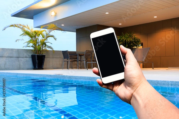 Obraz Hand hold Modern smartphone with blank screen at outdoor swimming pool and terrace upper deck. Copy space.