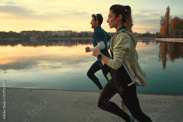 Fototapeta Young man and woman out for a run on the lake at the sunrise