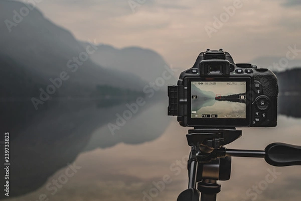 Obraz Camera on tripod at work on a misty lakeshore. Camera display. Taking pictures using the display.