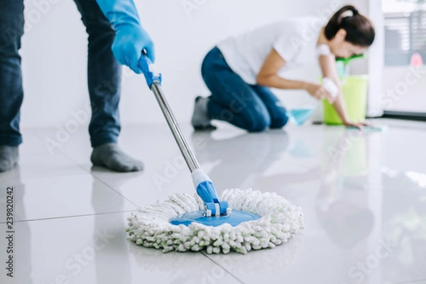 Obraz Housekeeping and cleaning concept, Young couple in blue rubber gloves wiping dust using mop and duster while helping cleaning on floor at home
