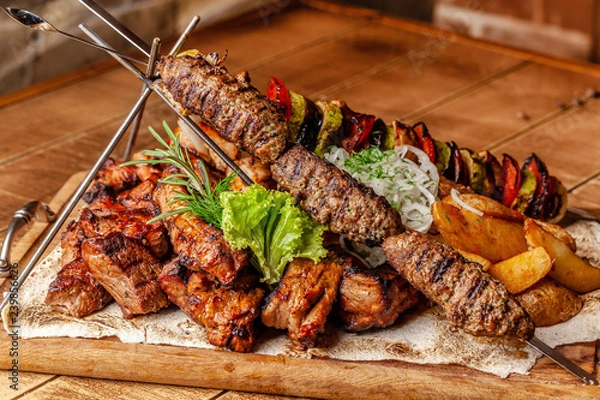 Obraz The concept of Georgian cuisine. Meat board with shashlik, grilled pork ribs, lulya kebab and shish kebab. Grilled french fries and grilled vegetables. Meat feed on a wooden board.