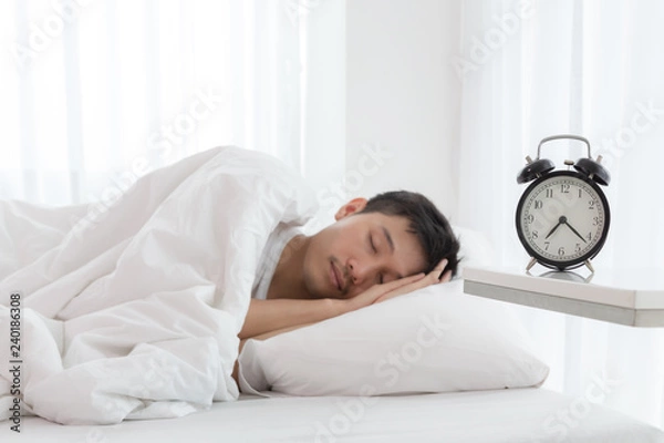 Obraz Young asian handsome man sleeping in his bedroom. Boy sleeping with alarm clock in foreground. The time is half pass 7 AM. Wake up in morning of working day concept.