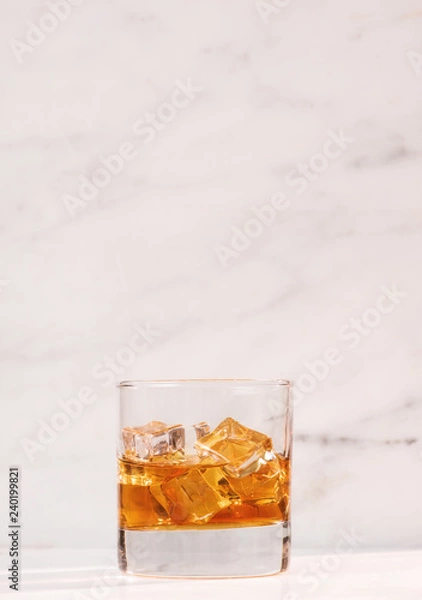 Fototapeta glass of whiskey or tea with ice on marble background vertical side view