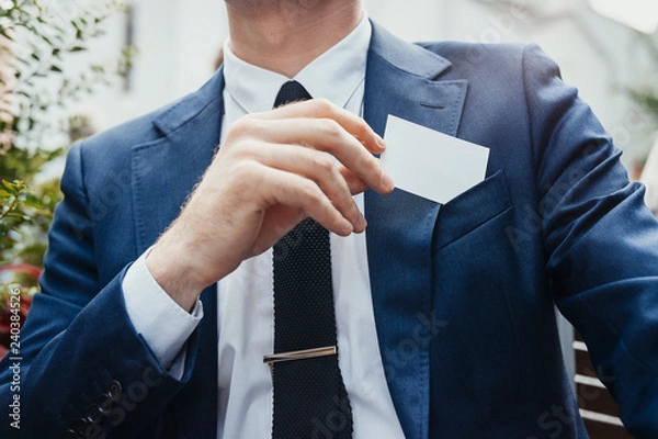Obraz Close up of businessman putting blank business card in his blue jacket pocket.
