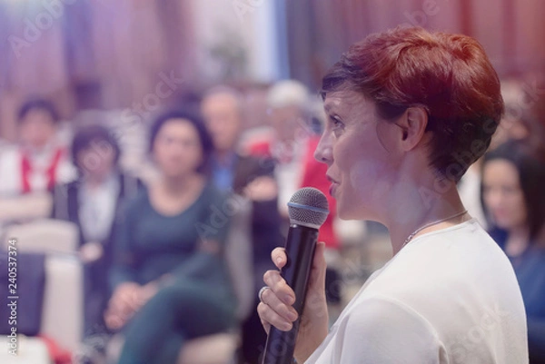 Fototapeta Beautiful business woman with microphone in her hand speaking at the  conference or seminar.