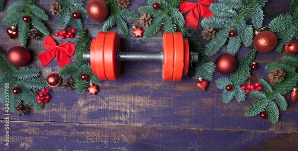 Obraz Christmas or New Year on a violet wooden background. Composition with dumbbells, gift, red and gold glass balls, fir tree branches for healthy lifestyle and sport