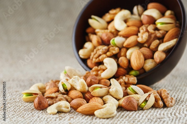 Fototapeta Mix of different nuts in a wooden cup against the background of fabric from burlap. Nuts as structure and background, macro. Top view.