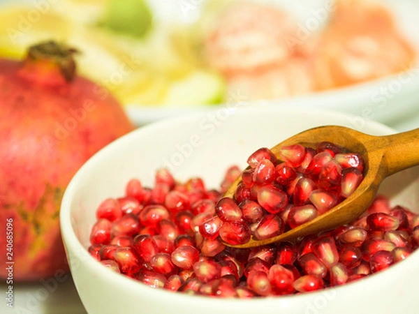 Obraz pomegranate seeds and wooden small spoon in white bowl.