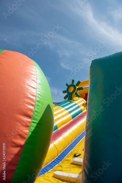 Fototapeta A giant colorful inflatable slider with joyful kids running up and down the slider in the fun park with happiness.
