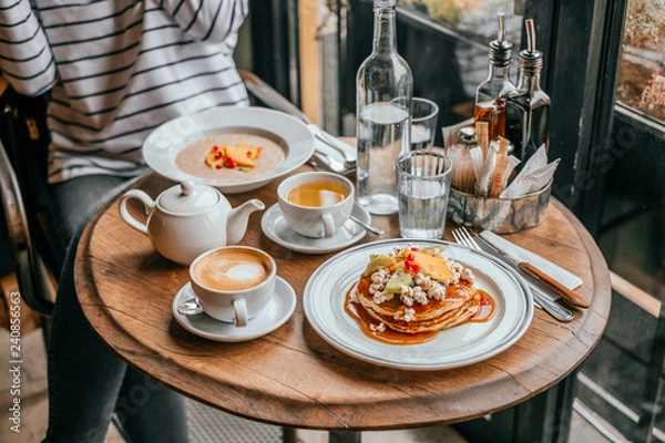 Fototapeta Perfect breakfast in the city cafe with pankakes, oatmeal, coffe and tea on the round wooden table.