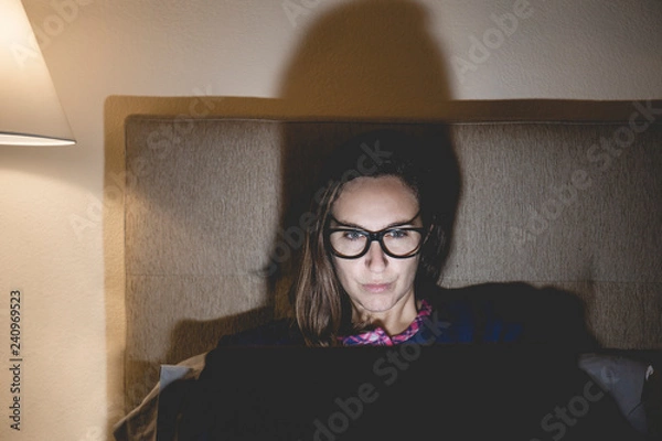 Fototapeta Pajama woman in bed at home bedroom working concentrated with the laptop at night or using the internet social network chat in the concept of dependence on technology